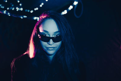 Portrait of confident young woman wearing sunglasses in illuminated restaurant