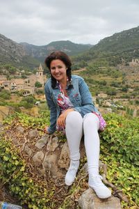 Portrait of young woman sitting on hill against valldemossa village and mountains