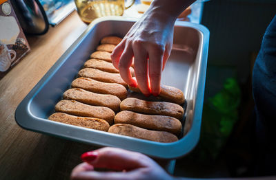 Human hand during a process of spreading lady fingers or spongecake in tray,process of tiramisu cake