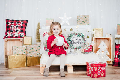 Wide angle view of smiling little girl wearing red christmas dress at home over christmas decoration