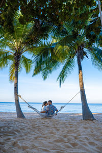 Couple embracing while sitting on hammock at beach