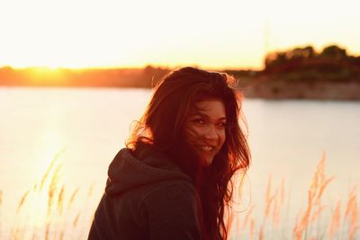 Portrait of happy beautiful woman by lake against sky during sunset