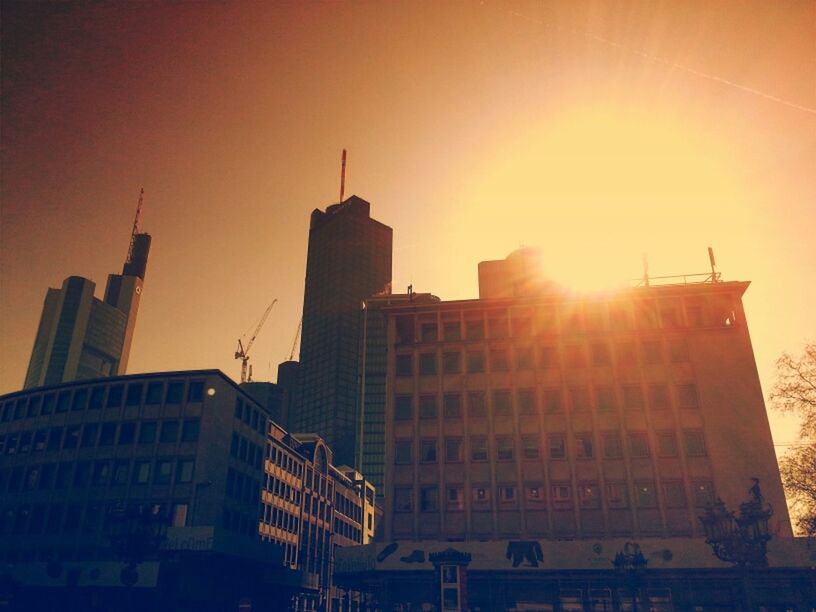 building exterior, architecture, sun, sunset, built structure, sunbeam, sunlight, city, lens flare, orange color, tower, skyscraper, tall - high, low angle view, sky, building, bright, development, outdoors, office building