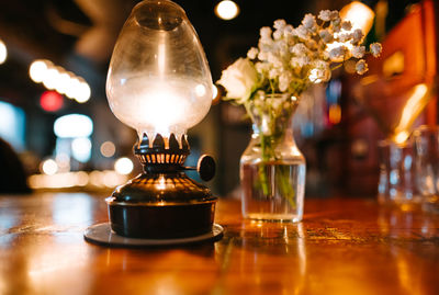 Close-up of illuminated oil lamp by flower vase on table