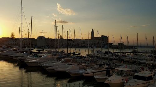 Sailboats moored in harbor at sunset