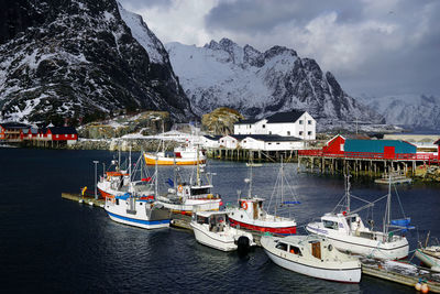 Sailboats moored on sea by snowcapped mountains against cloudy sky