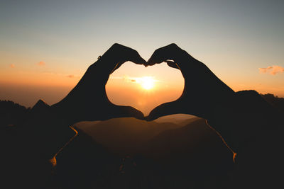 Fingers forming heart shape at dusk