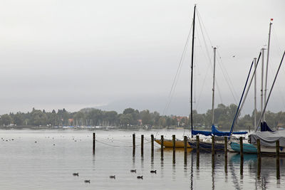 Boats in harbor at lake against sky