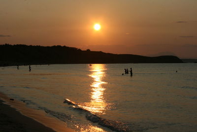 Silhouette people on beach against sky during sunset