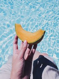 Midsection of person holding a melon slice on swimming pool