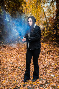 Young woman holding distress flare while standing in forest during autumn