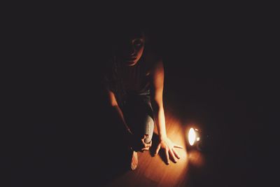 High angle portrait of young woman sitting by illuminated flashlight on floorboard