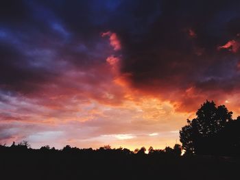 Silhouette trees against dramatic sky during sunset