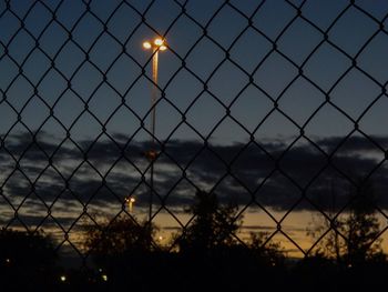 Close-up of illuminated chainlink fence against sky during sunset