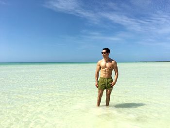 Shirtless man standing in sea on sunny day