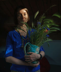 Portrait of young woman holding camera while standing against wall