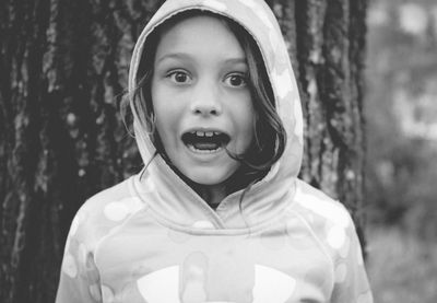 Portrait of shocked girl in hood clothing against tree