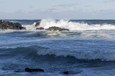 Waves splashing on shore against sky