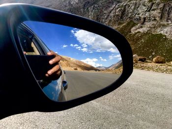 Cropped hand of person photographing reflecting on car side-view mirror