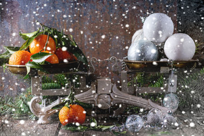 Close-up of oranges and baubles on weight scale during snowfall