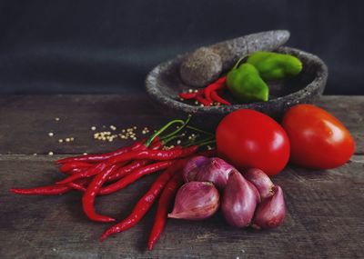 Close-up of tomatoes, chilies, onions and mortar made from stone on table