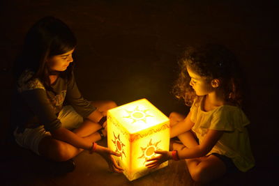 Girls sitting by illuminated lighting equipment in darkroom