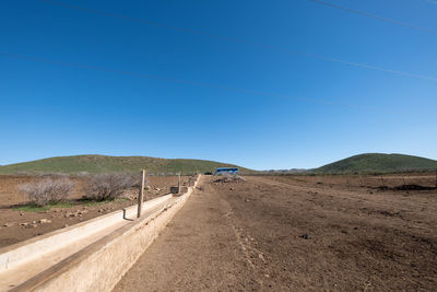 Road leading towards mountains against clear blue sky