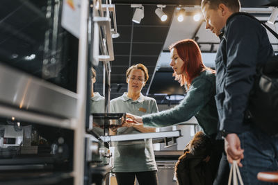 Female sales clerk assisting mature couple in buying microwave oven at electronics store