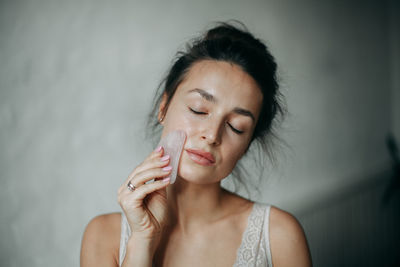 Brunette woman 30 years old doing face massage with a gouache scraper