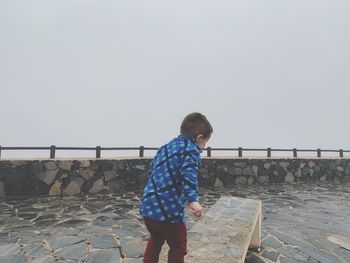 Side view of boy standing on footpath against sky during foggy weather