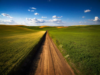 Dirt road amidst field against sky