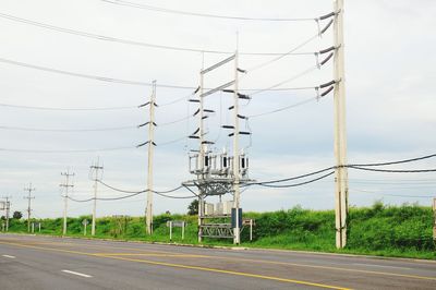 Electricity pylons by road against sky