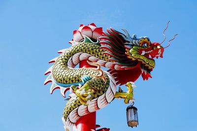 Low angle view of dragon sculpture against clear blue sky