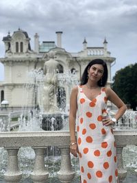 Portrait of woman standing against fountain in city