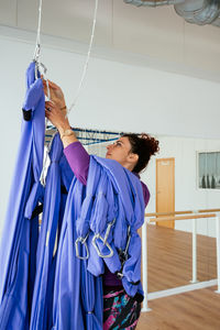 Side view of female trainer hanging swings with carbines for aerial yoga while preparing for class in light spacious studio