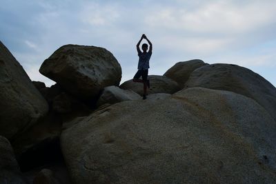 Rear view of man on rock at beach against sky