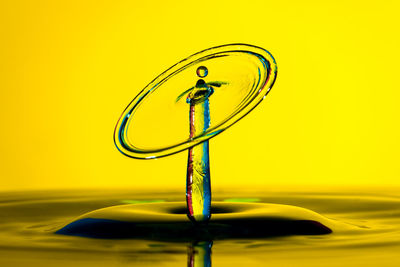 Close-up of drop splashing on water against yellow background