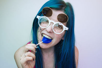 Portrait of woman wearing sunglasses while eating candy against wall