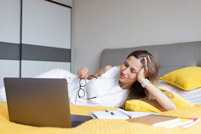 Smiling woman talking on video call while lying on bed at home