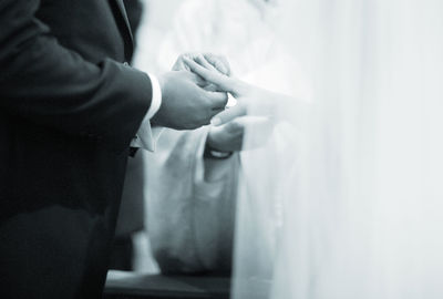 Midsection of groom putting ring in bride finger