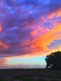 Scenic view of landscape against cloudy sky at sunset