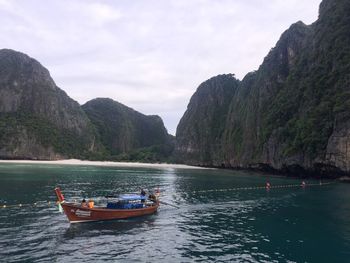 Boats on sea by mountains against sky