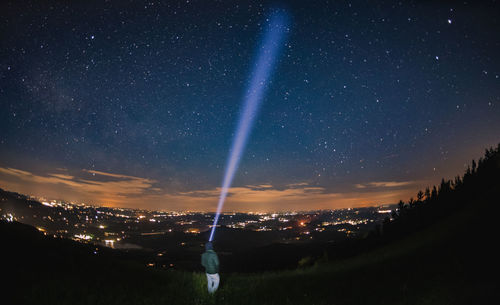 Rear view of person with flashlight on mountain against star field