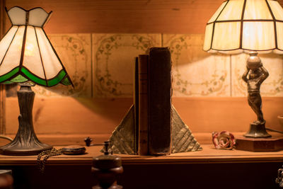 Close-up of illuminated electric lamps and old books on sideboard at home