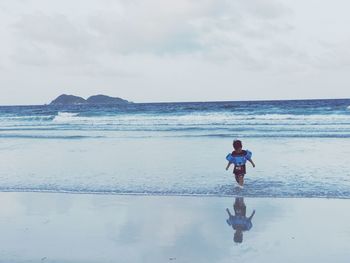 Boy walking on shore against sky at beach