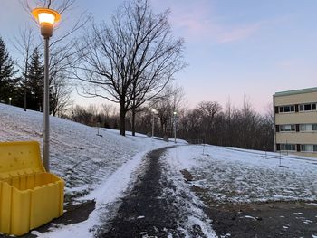 Snow covered road by buildings against sky