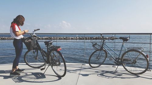 Side view of woman standing with bicycles on promenade against sky