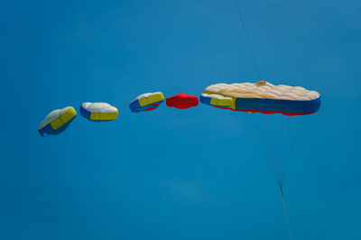 Low angle view of parachutes flying against blue sky