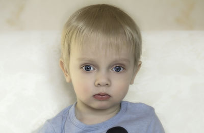 Close-up portrait. a serious little blonde boy in a blue t-shirt looks into the camera.