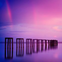 Wooden posts in sea against sky at sunset